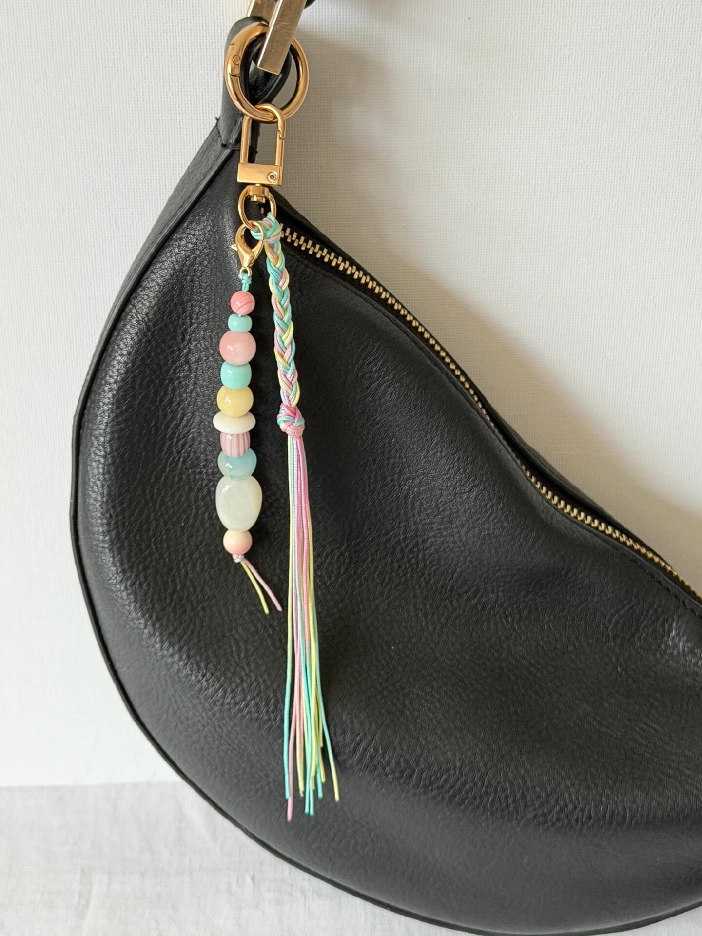 pastel chunky bead bag charm in pink, blue, lemon and white with a braided tassel in nylon cords in pink, blue and yellow displayed worn on a bag