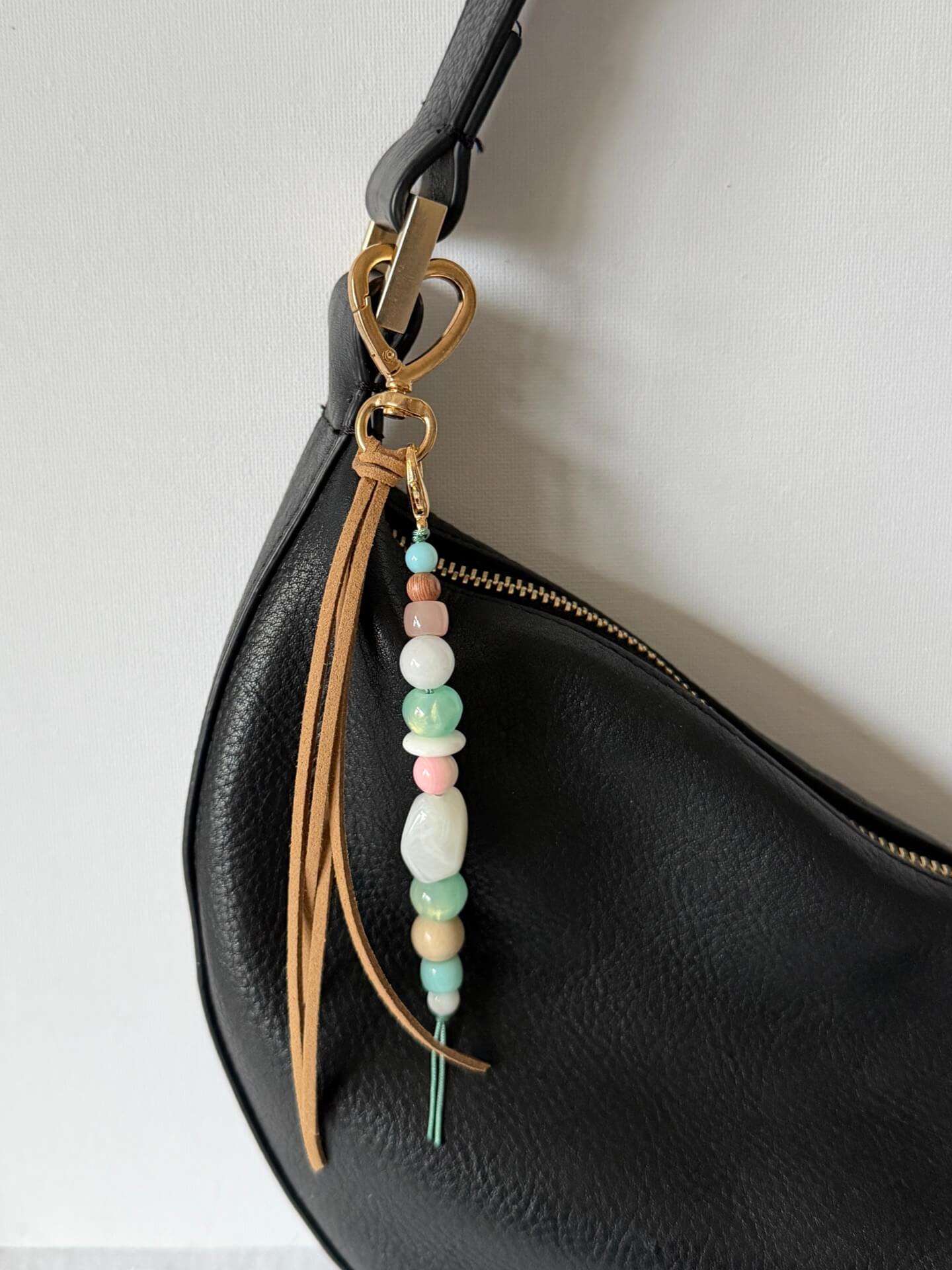 faux suede tassel beaded bag charm with chunky beads in pink, aqua, white and beige attached to a black bag