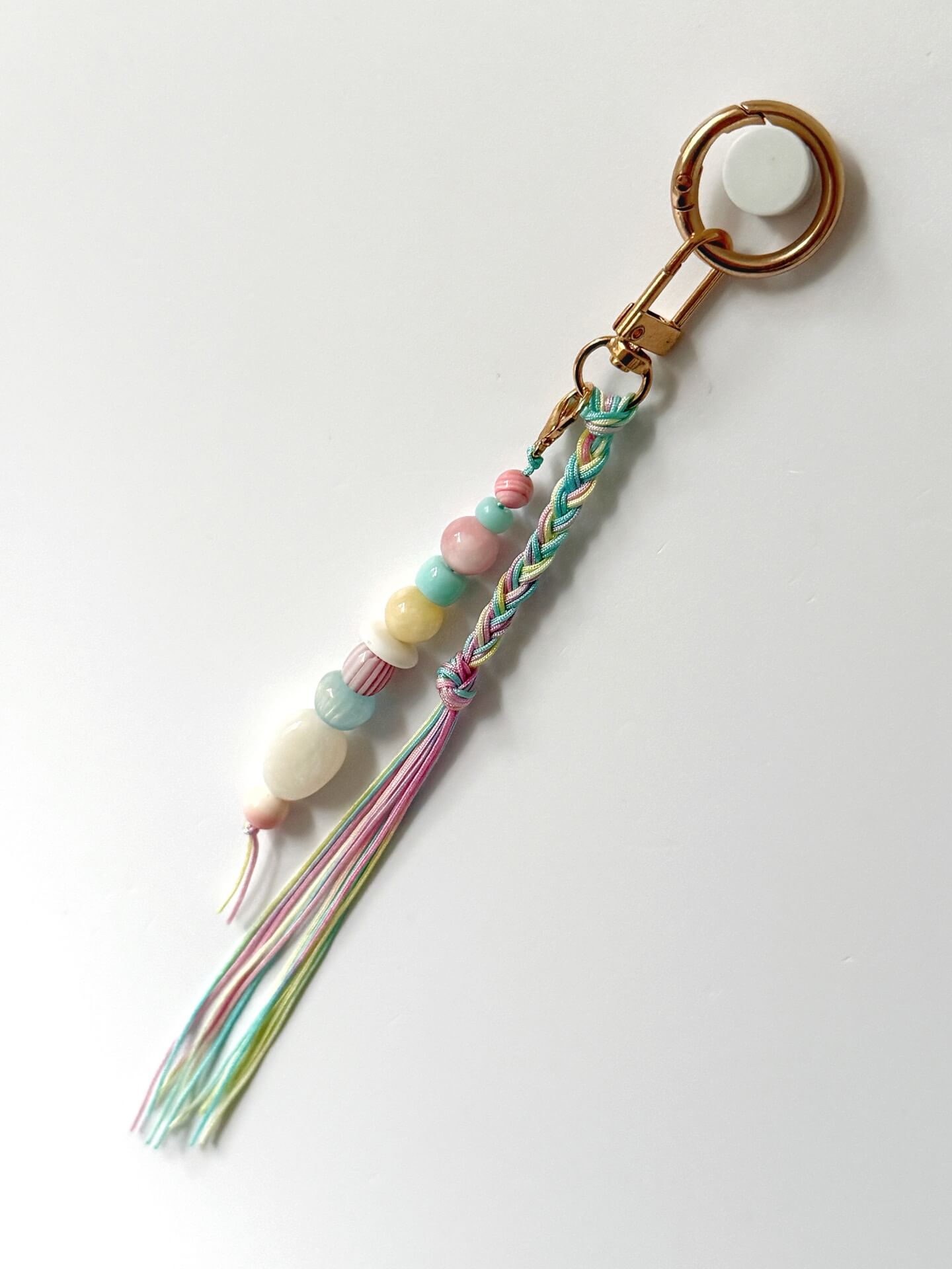 pastel chunky bead bag charm in pink, blue, lemon and white with a braided tassel in nylon cords in pink, blue and yellow against a white background
