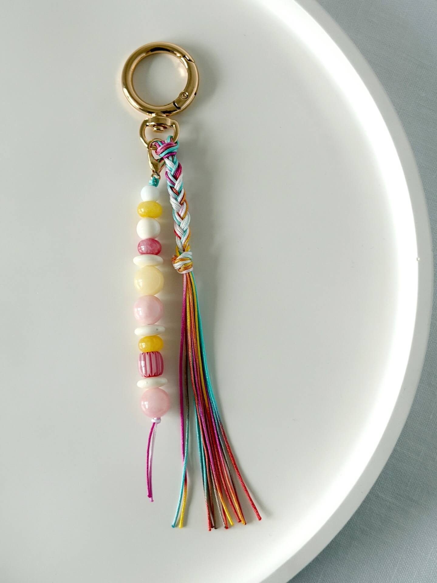 beaded bag charm with red, yellow, white and pink beads with a rainbow coloured nylon braided tassel 