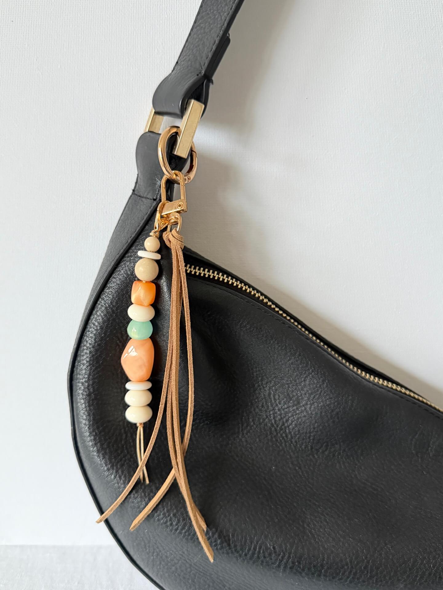 gold bag charm or key ring with long beige faux suede tassel and resin and stone beads in beige, orange, cream and aqua displayed on a black bag