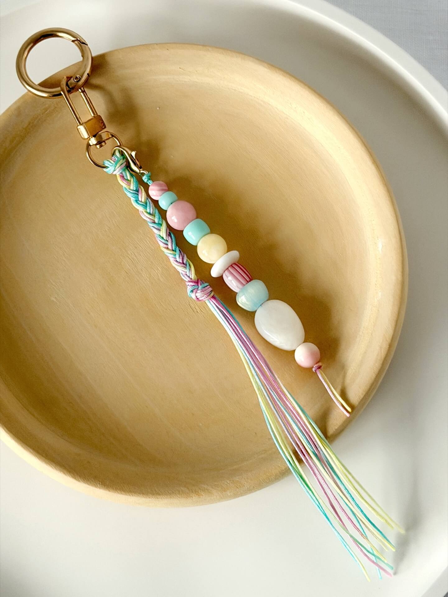 pastel chunky bead bag charm in pink, blue, lemon and white with a braided tassel in nylon cords in pink, blue and yellow displayed on a wooden plate
