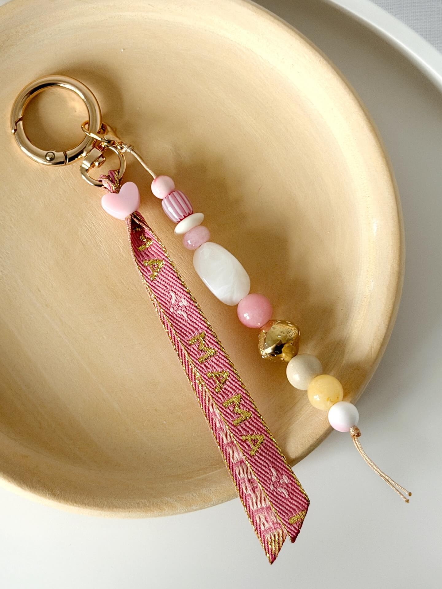 beaded bag charm with Momma printed ribbon and pink, yellow, white, red and gold beads displayed on a wooden plate