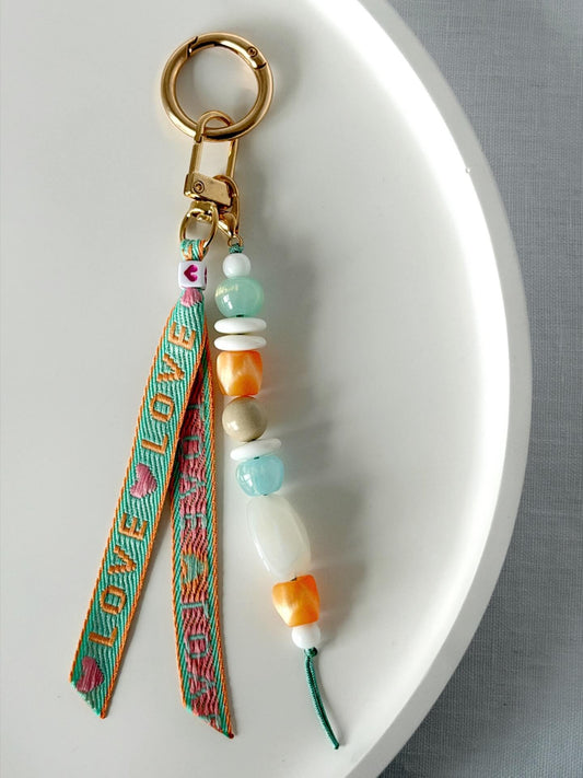 beaded bag charm with a love embroidered ribbon and aqua, white and orange chunky resin beaded on a gold clasp