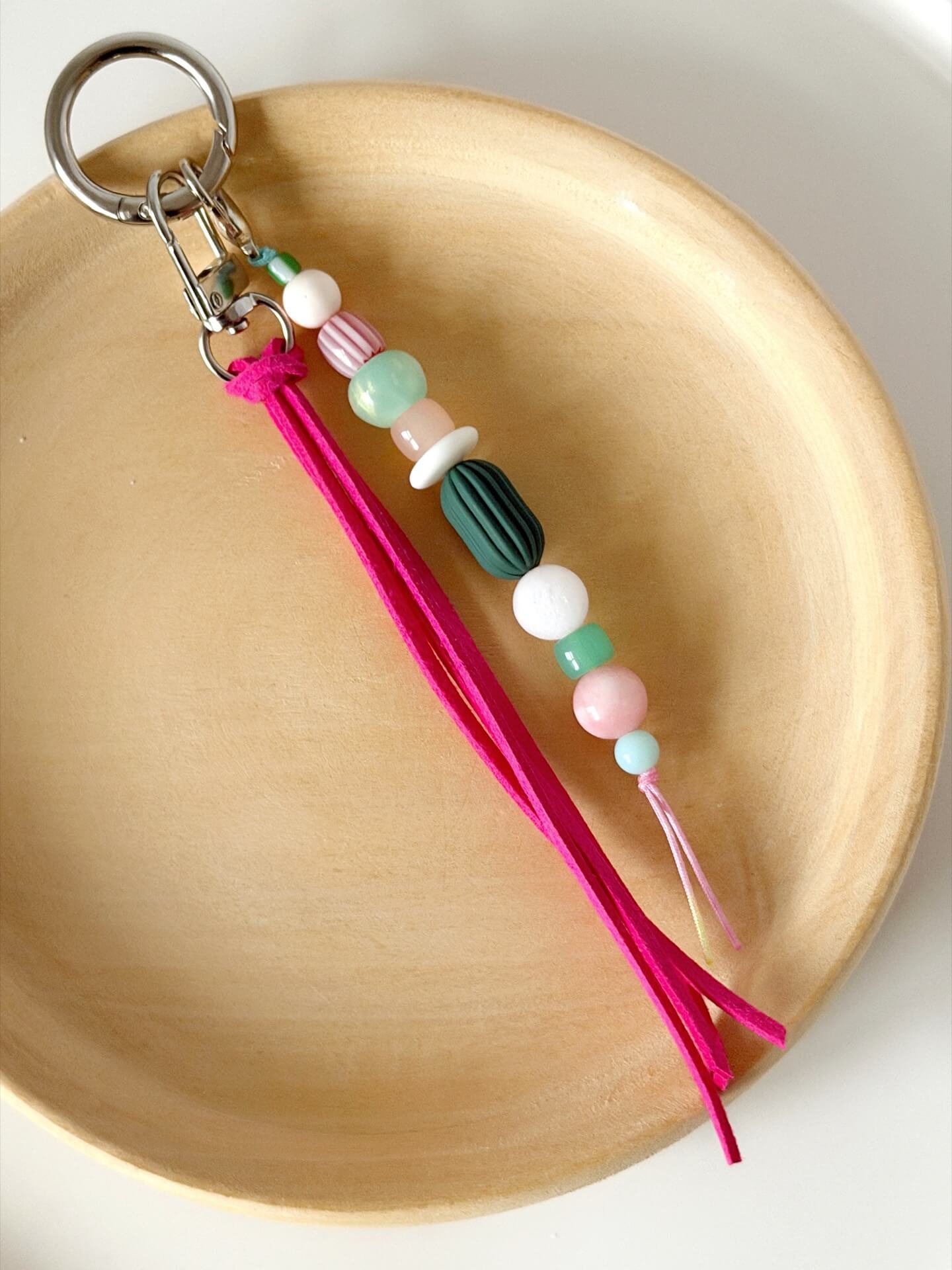 beaded bag charm with neon pink suedette tassel and chunky pink, green and white beads displayed on a wooden plate