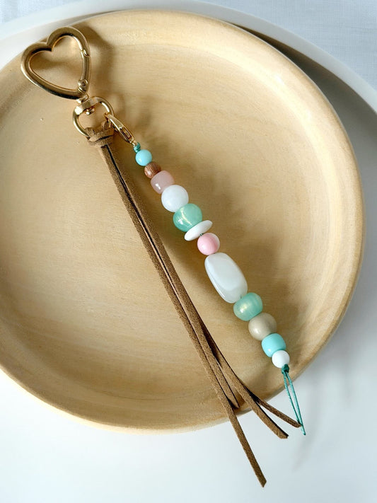 faux suede tassel beaded bag charm with chunky beads in pink, aqua, white and beige displayed against a wooden plate