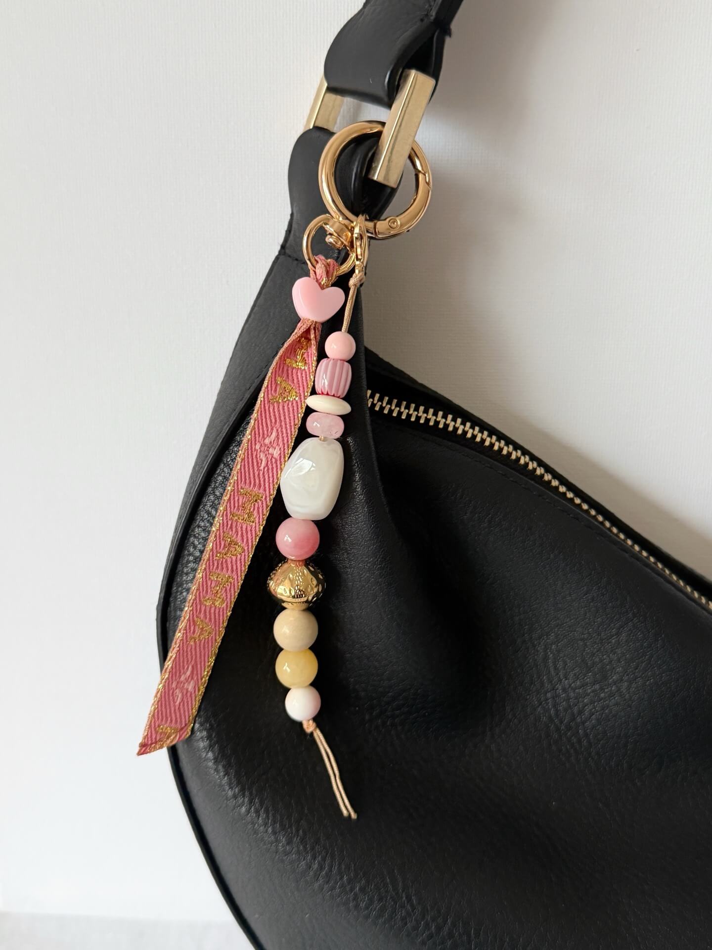 beaded bag charm with Momma printed ribbon and pink, yellow, white, red and gold beads displayed hung on a black bag