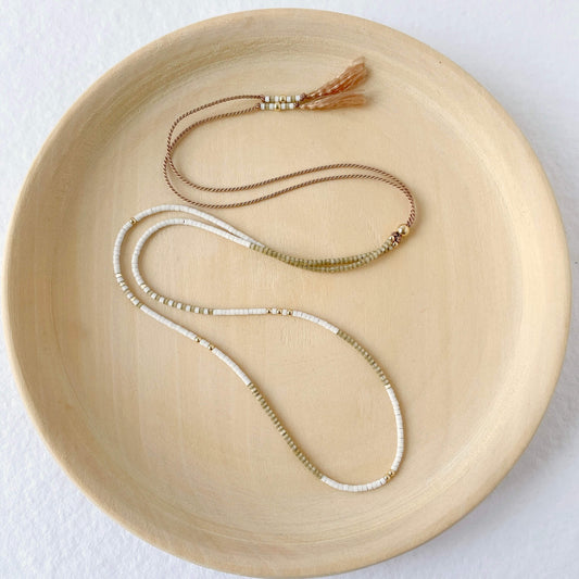 a beige and white delicate beaded silk necklace with gold sliding bead on a wooden plate