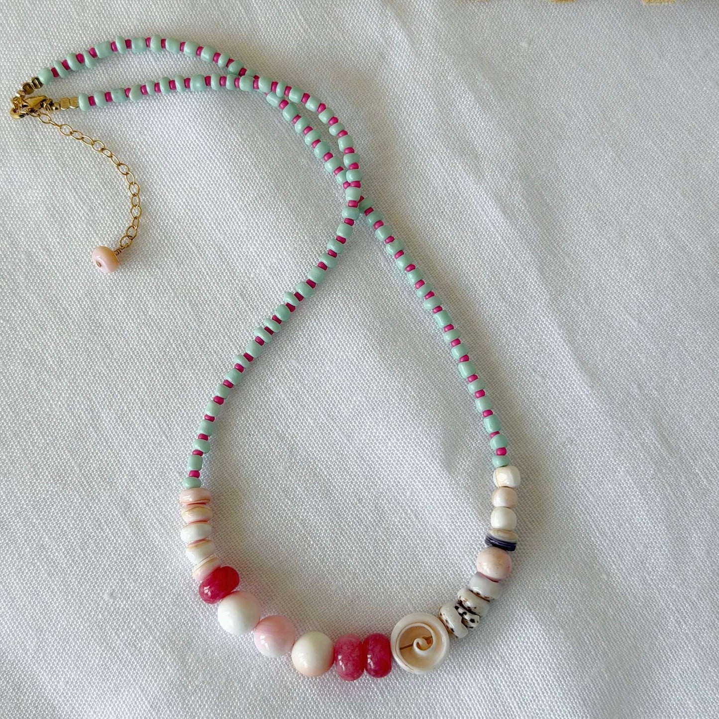 Beaded necklace with blue, pink and purple beads on a light fabric background