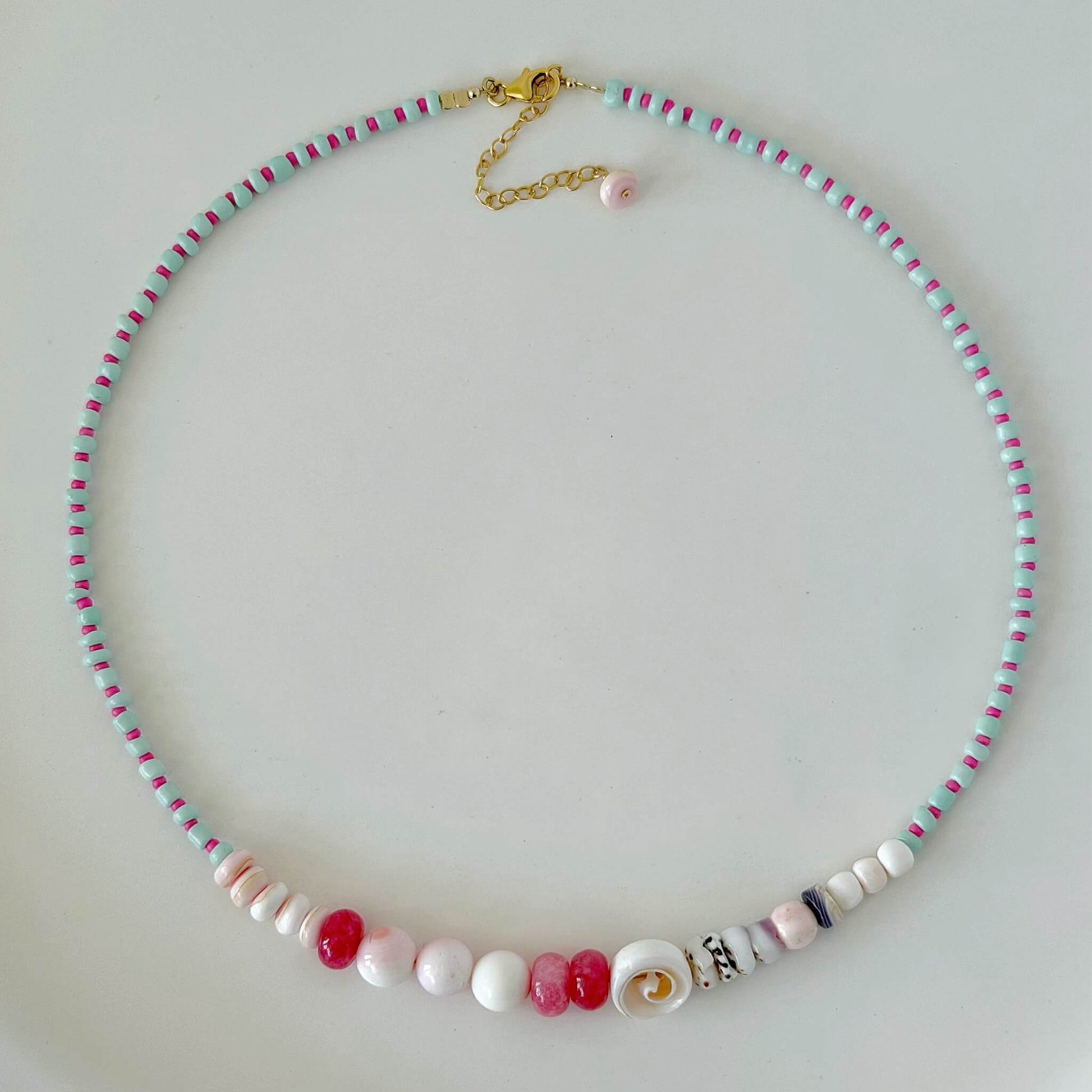 Aqua, pink, red and purple glass and shell bead necklace with gold fill clasp on a white surface