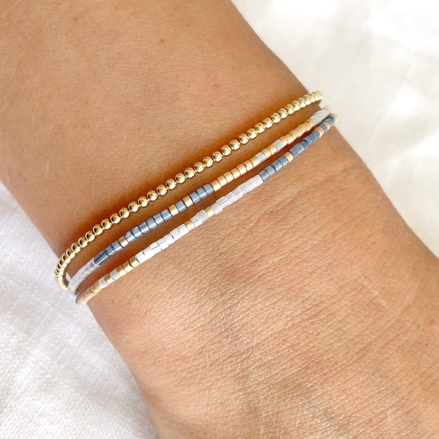 Double wrap friendship bracelet with blue, white and champagne beads shown worn on wrist with a gold bead bracelet