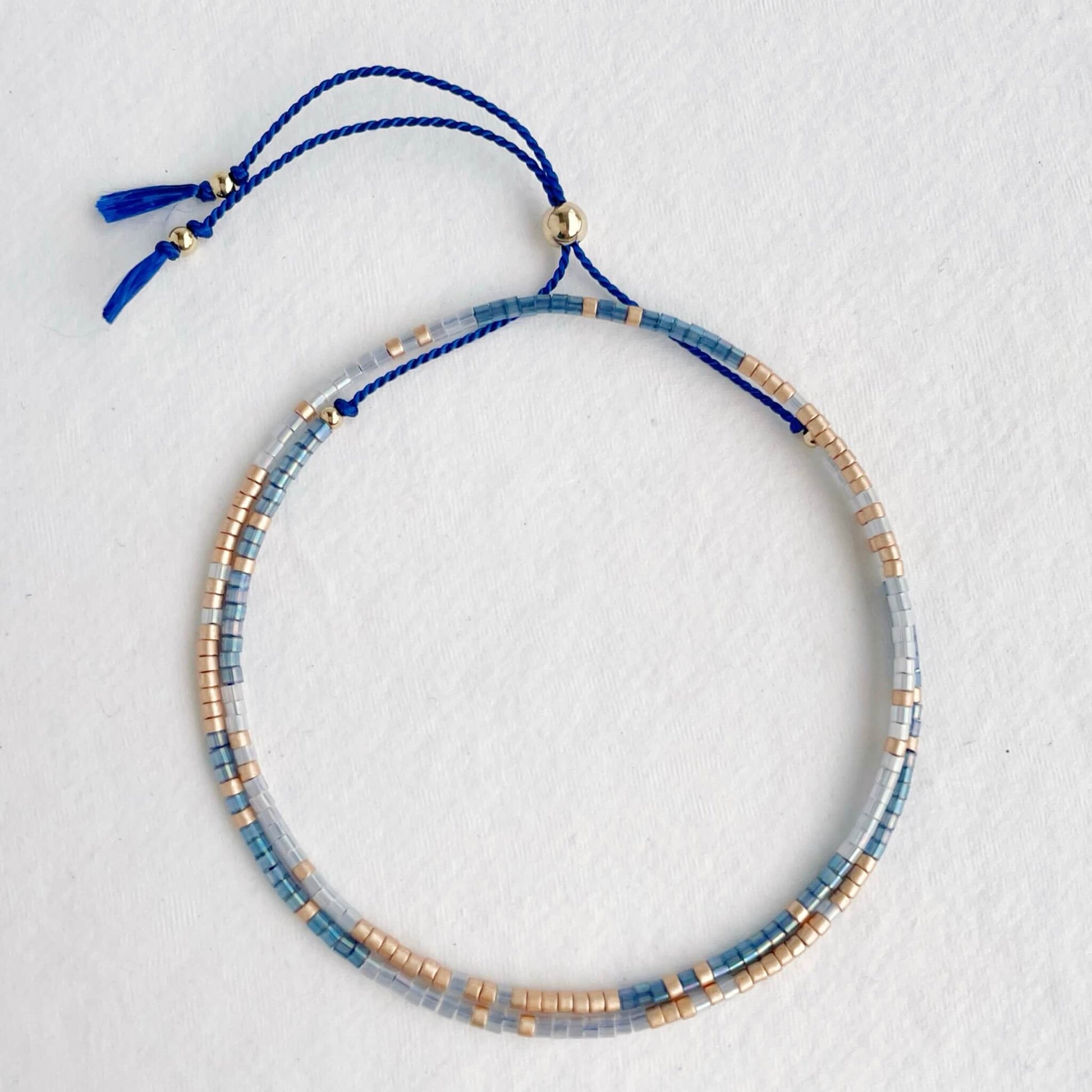 Double wrap friendship bracelet with blue, white and champagne beads and gold slider bead against white background