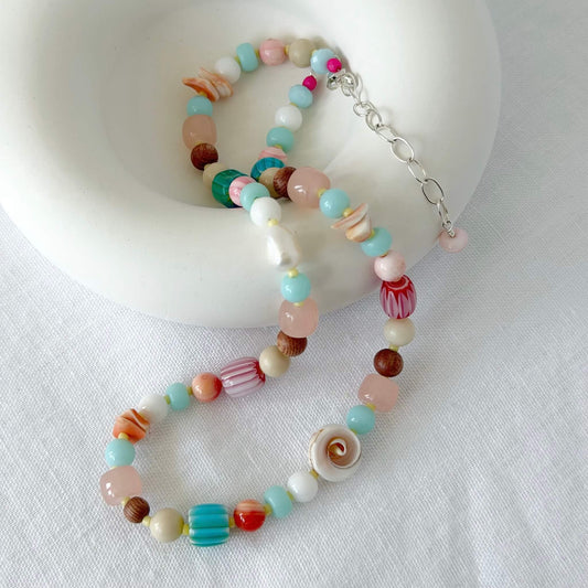 Chunky handmade beaded necklace with aqua, turquoise, pink, pearl, shell and wood beads with sterling silver clasp draped over a white bowl