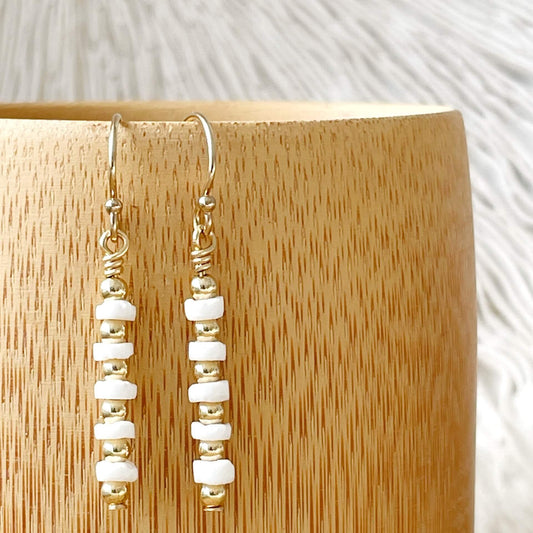 Pair of gold and white beaded earrings on a wooden stand.