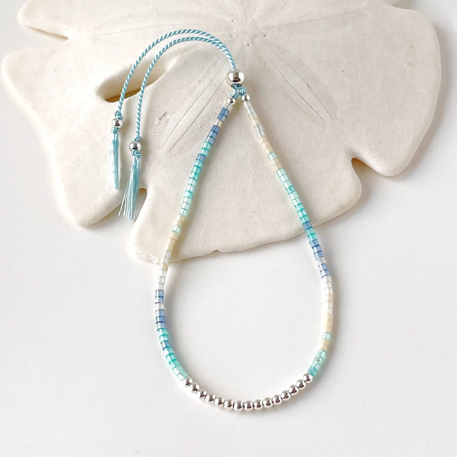 dainty beaded bracelet with blue, aqua and beige glass beads and sterling silver accents on a pale blue silk cord