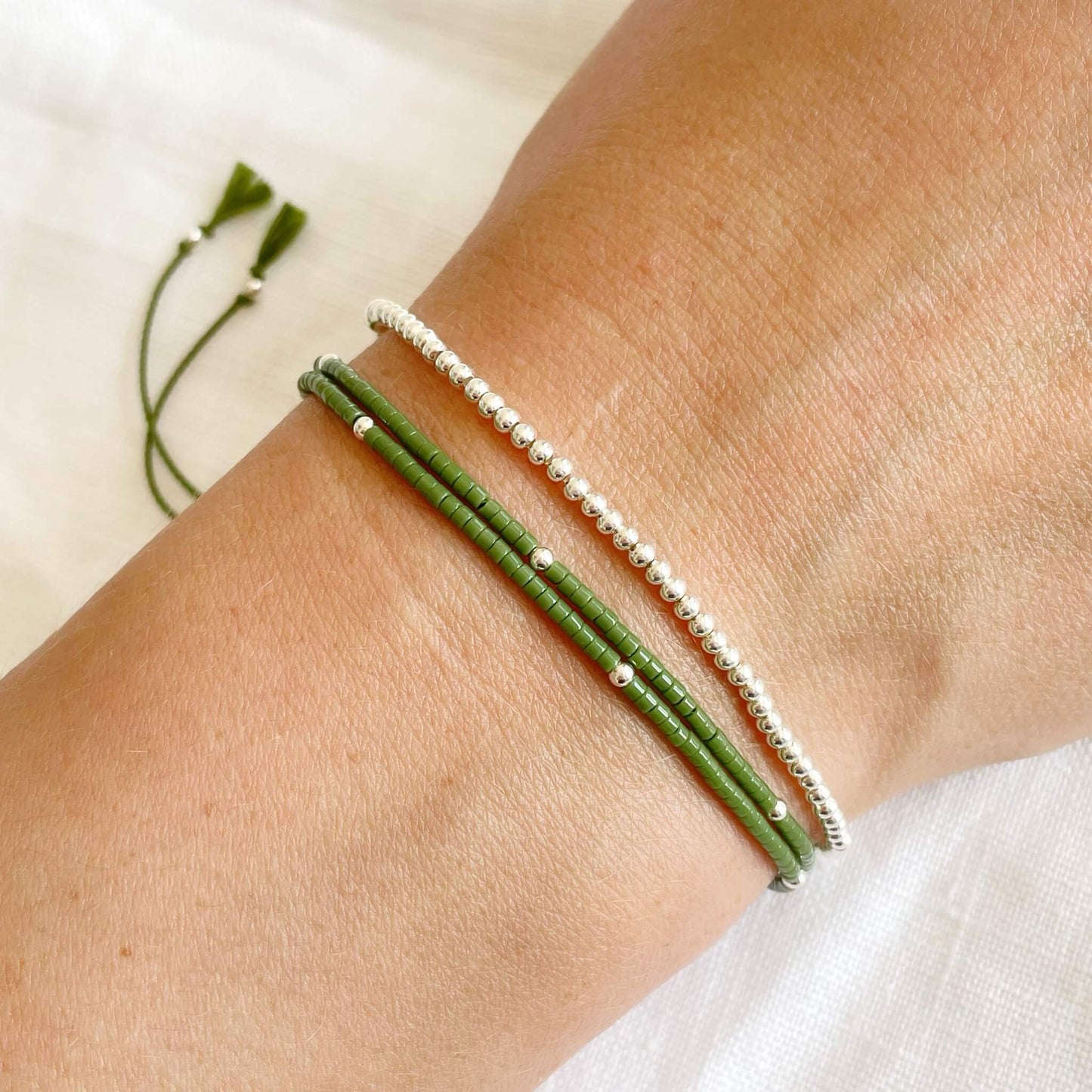 dainty sterling silver beaded bracelet worn with a khaki and silver double wrap bracelet shown on a wrist