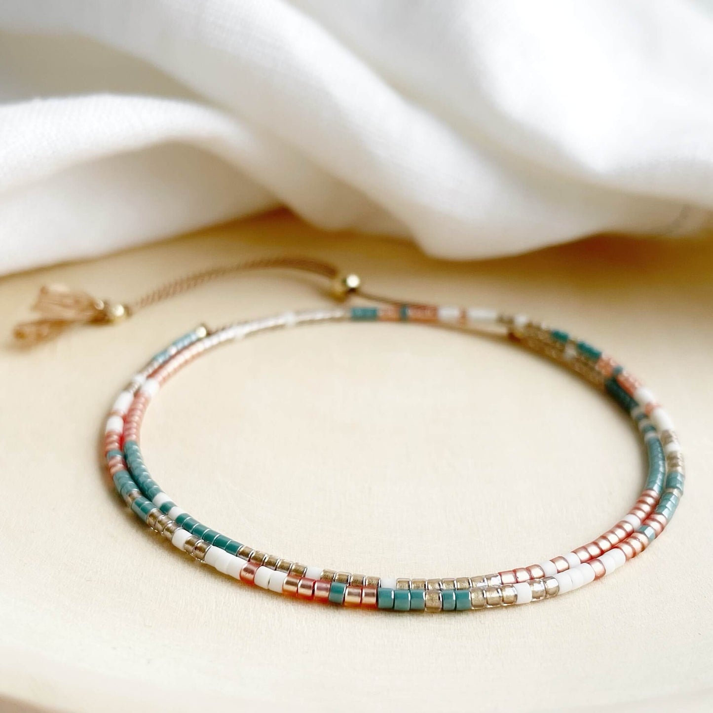 dainty beaded double wrap bracelet in teal, golden orange and pale gold with gold fill on a beige silk cord