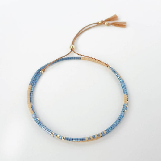 Blue beaded and beige double wrap bracelet on a beige silk with tassels on a white background