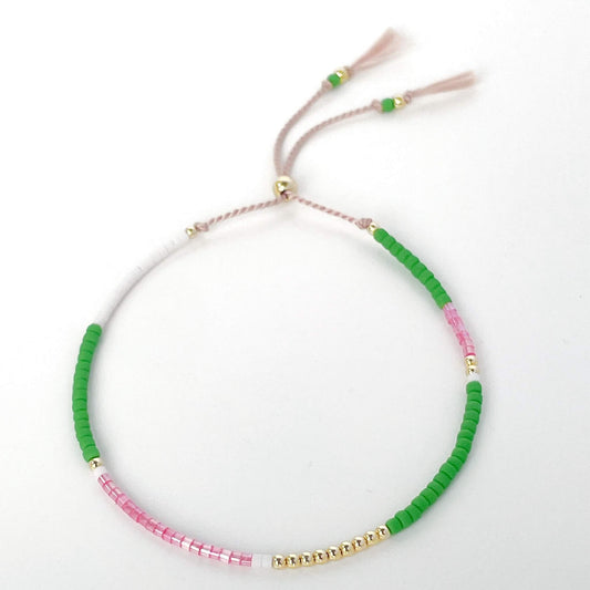 Beaded bracelet with green, pink, and gold beads on a pale pink silk cord with tassels