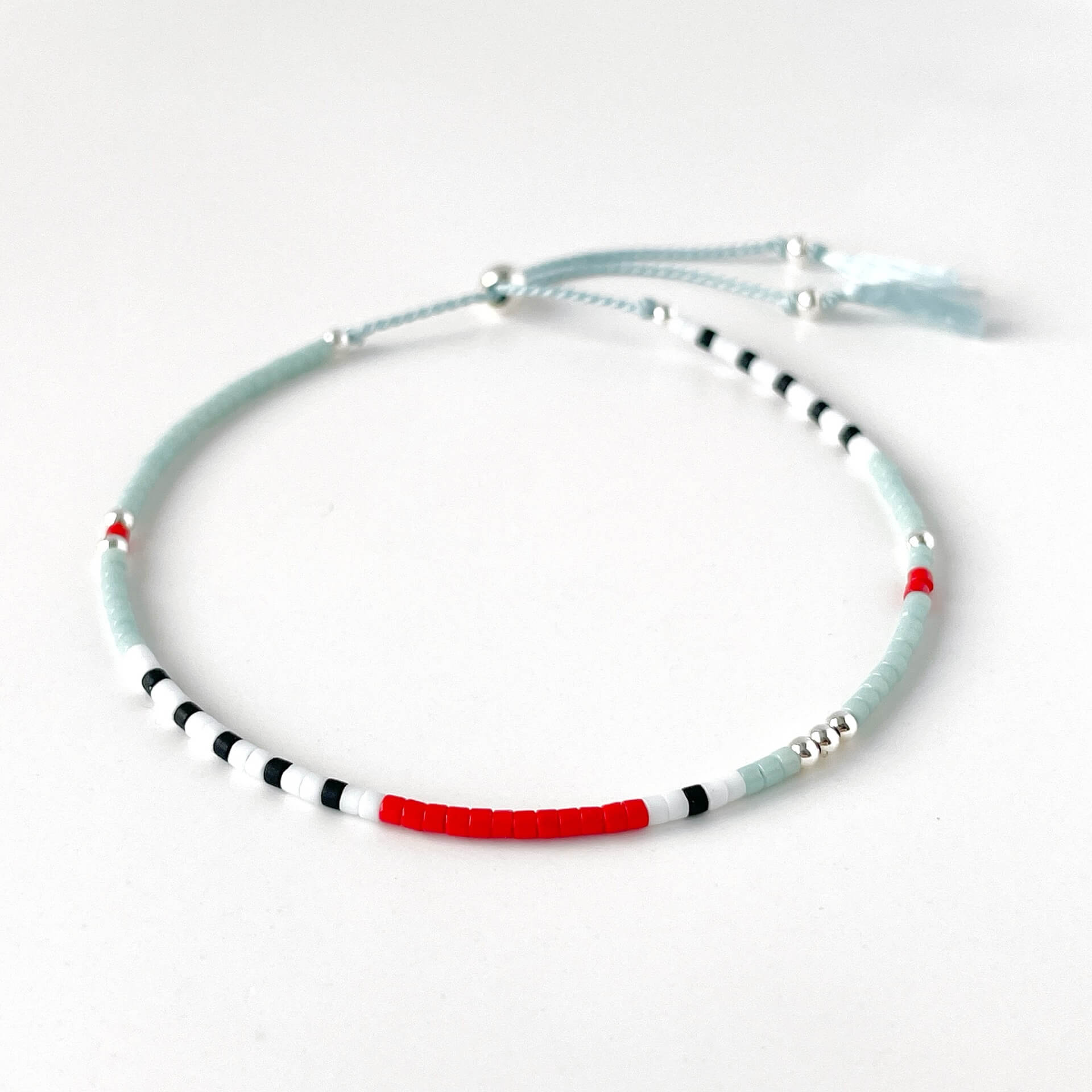 Nautical glass bead bracelet with pale blue, white, black and red beads and sterling silver accents on silk cord on a white background