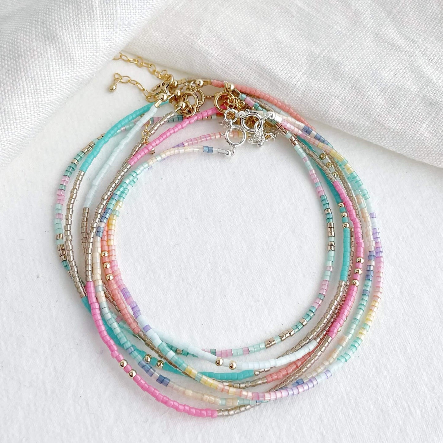 a collection of 7 tiny beaded vibrant anklets displayed together