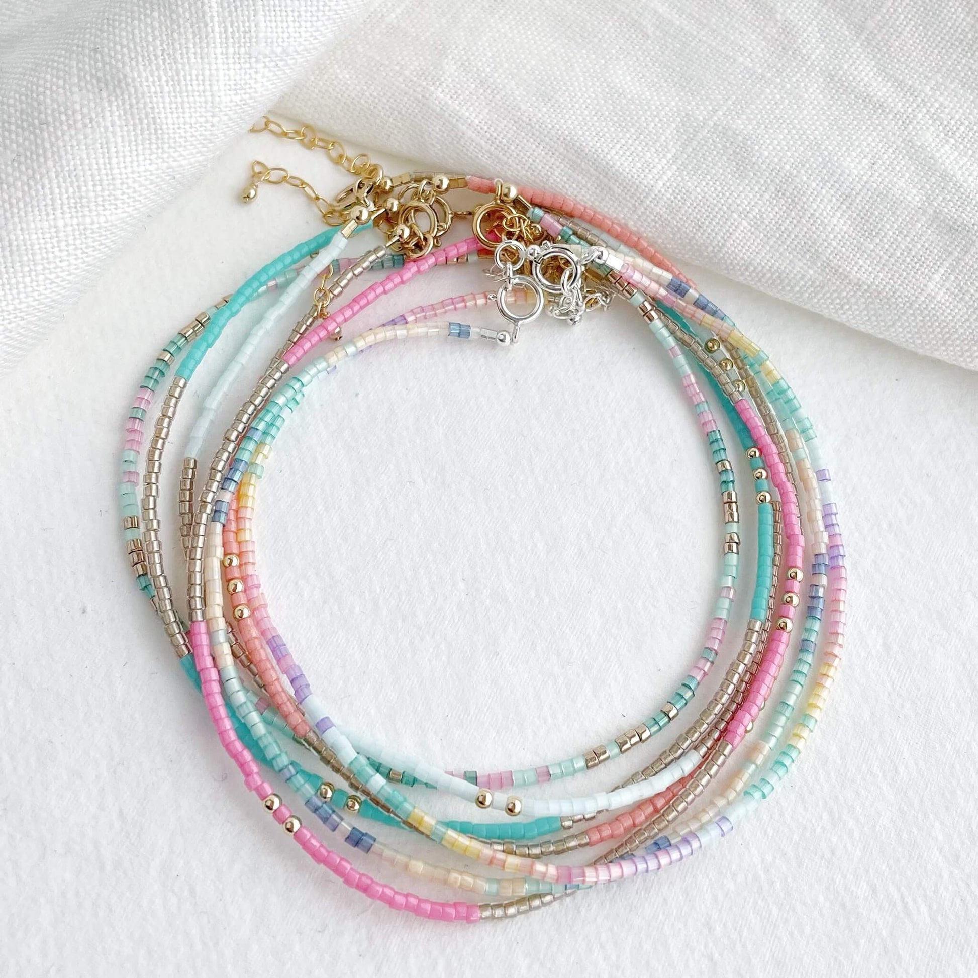 a collection of 7 tiny beaded vibrant anklets displayed together