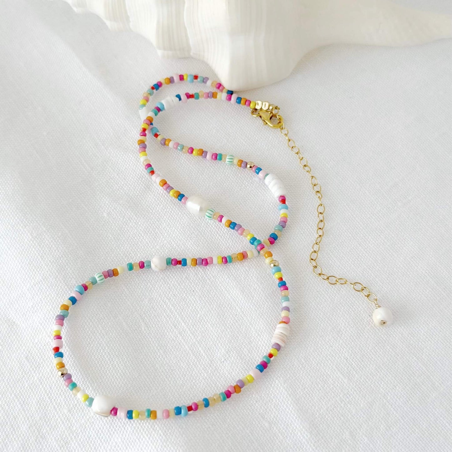 Multicolour glass bead and shell necklace with gold fill clasp and extender chain on a white flat lay surface with a white shell