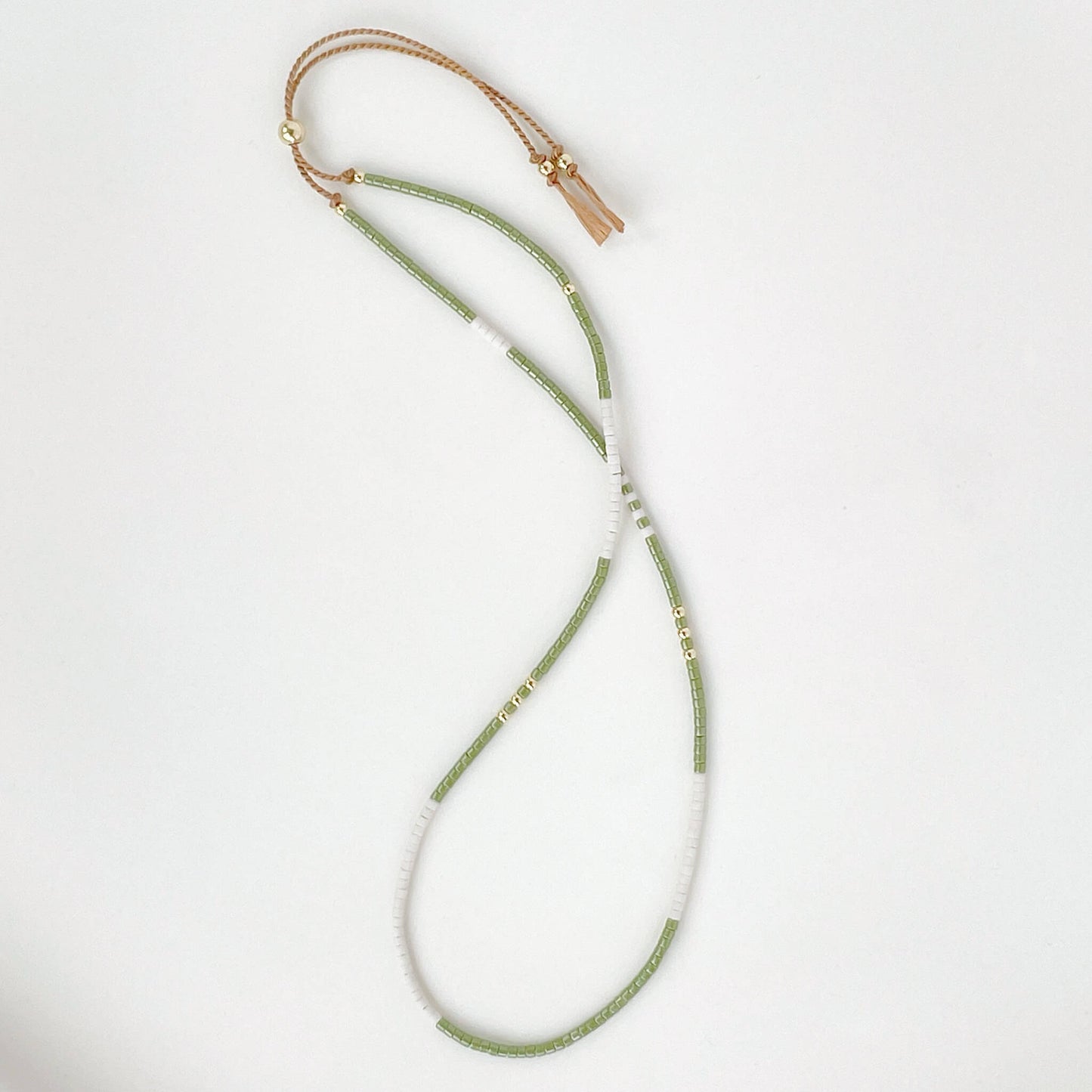Beaded bracelet with green beads and gold clasp on a white background