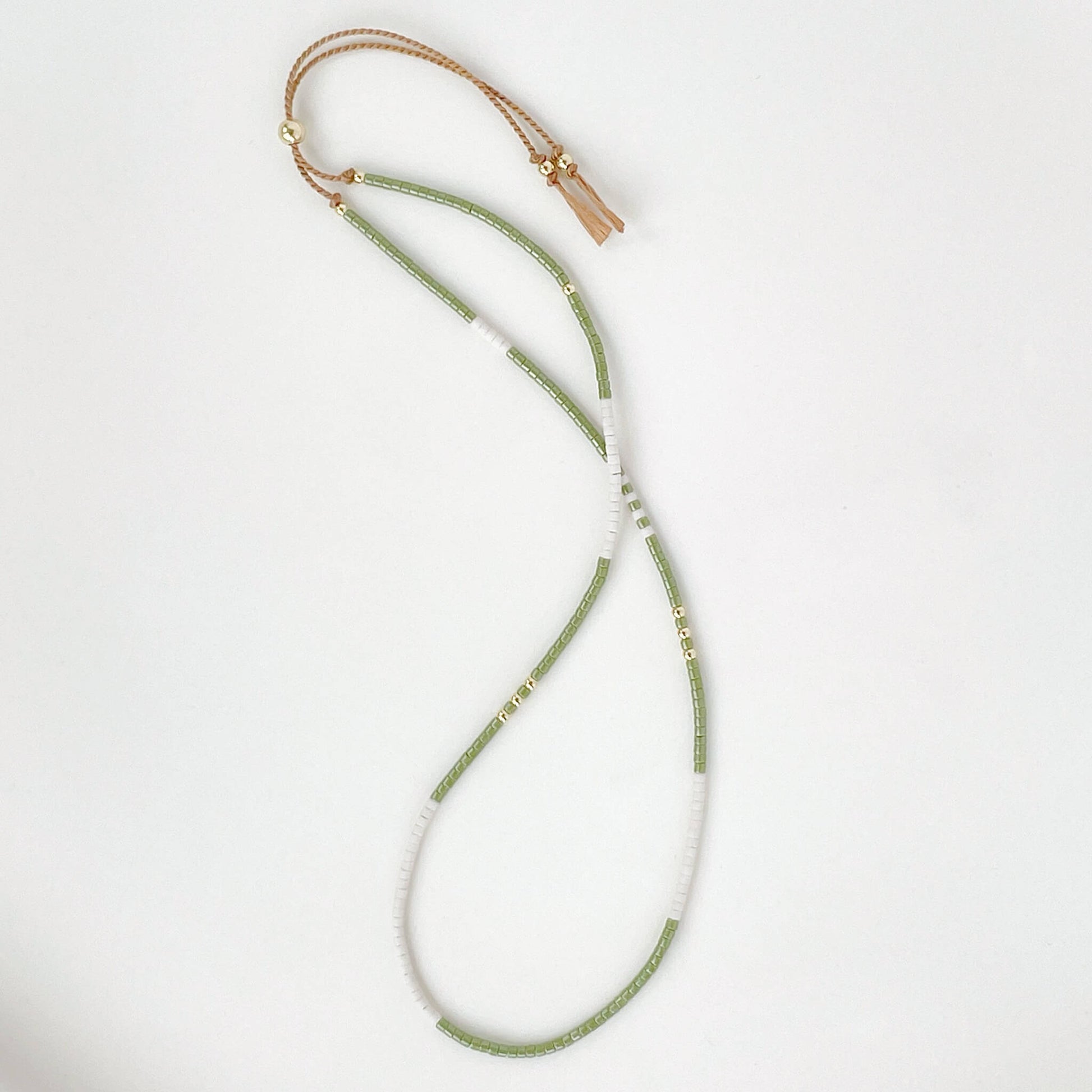Beaded bracelet with green beads and gold clasp on a white background