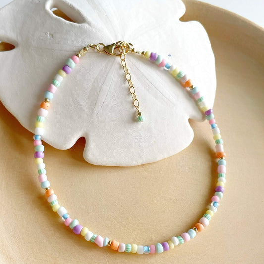 Colourful anklet with pastel coloured glass beads and gold fill accents draped over a white sand dollar