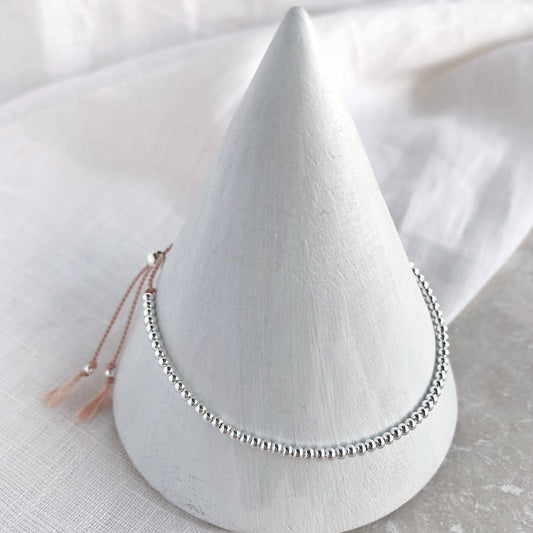Dainty beaded bracelet on soft pink silk with 2mm sterling silver beads displayed on a cone