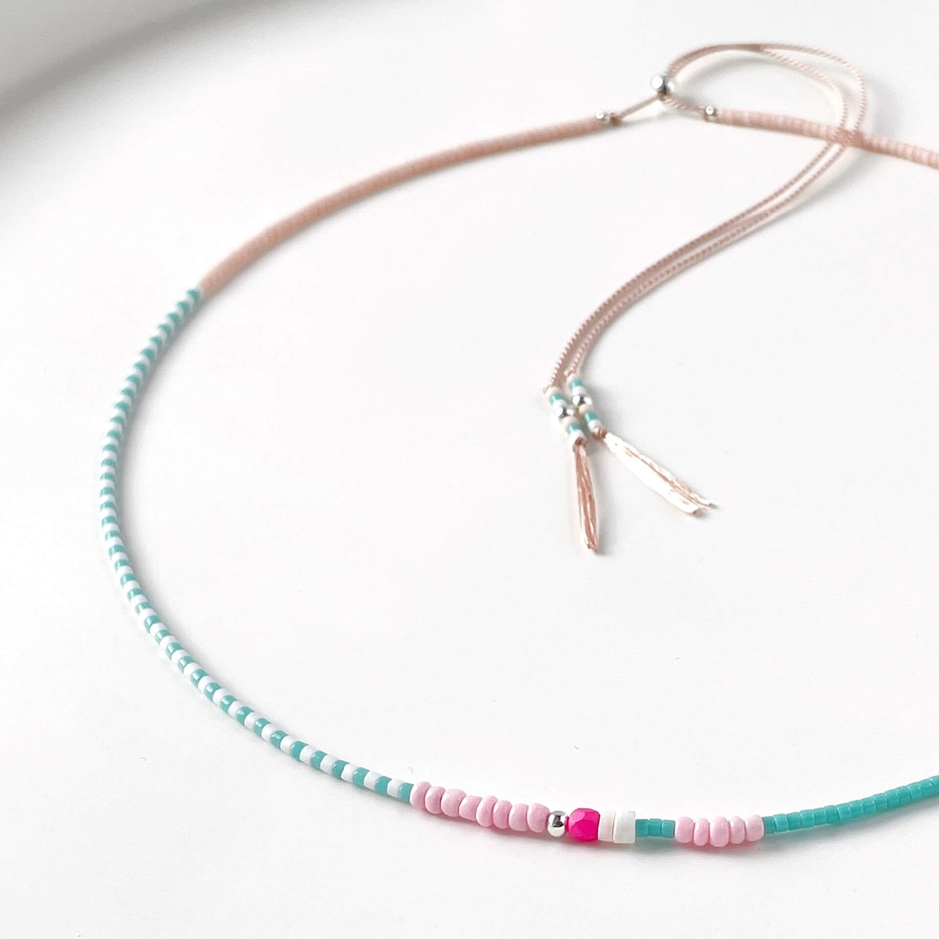 Necklace with turquoise and pink beads on a pale pink silk cord on a white background