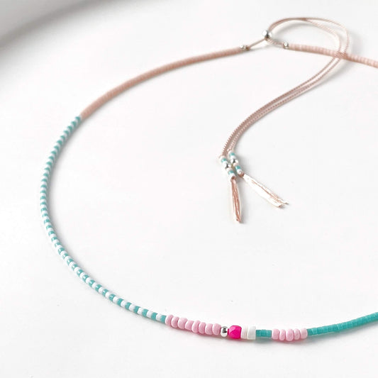 Necklace with turquoise and pink beads on a pale pink silk cord on a white background