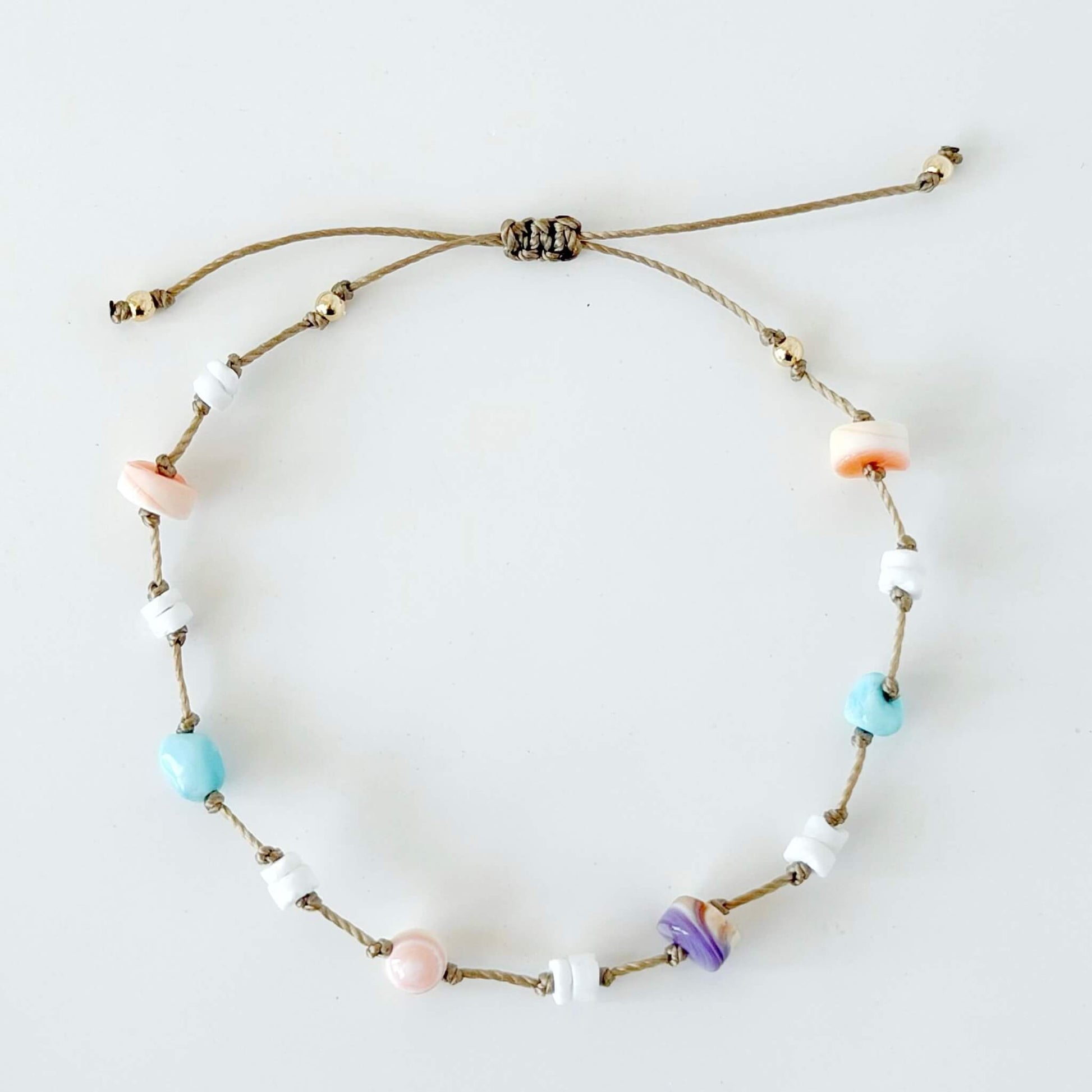 Beige knotted nylon cord bracelet with Larimar gemstone, pink conch shell, orange shell and purple wampum shell beads on a neutral surface