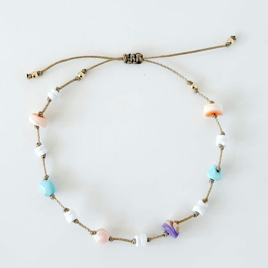 Beige knotted nylon cord bracelet with Larimar gemstone, pink conch shell, orange shell and purple wampum shell beads on a neutral surface