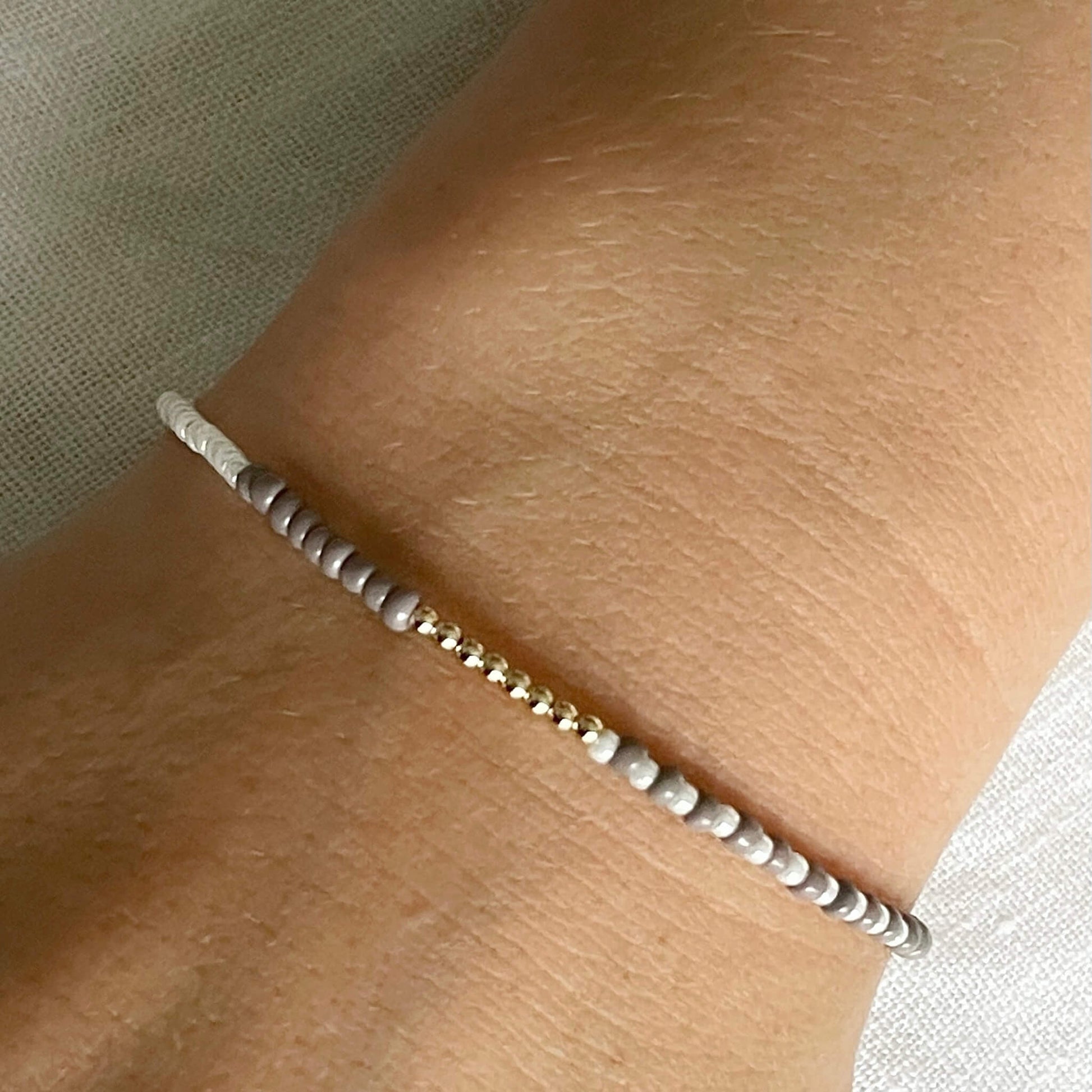 Beige & white glass beaded bracelet with gold fill accents worn on the wrist