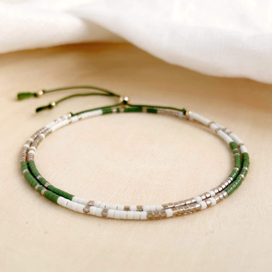Troop double wrap bracelet with khaki green, white and gold glass beads on olive green silk displayed against a wooden background