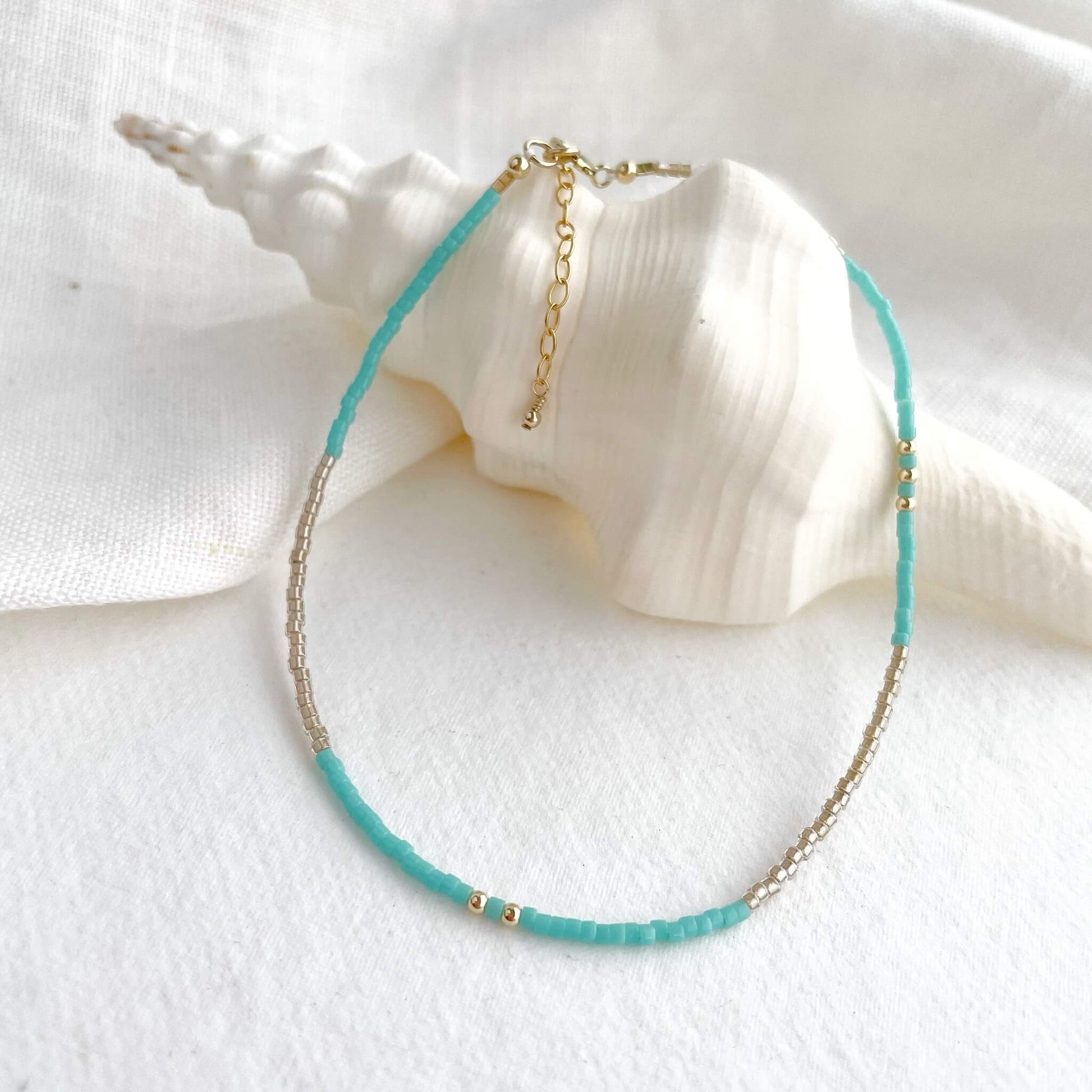 anklet with turquoise and golden Japanese glass beads and gold fill accents displayed draped over a white shell