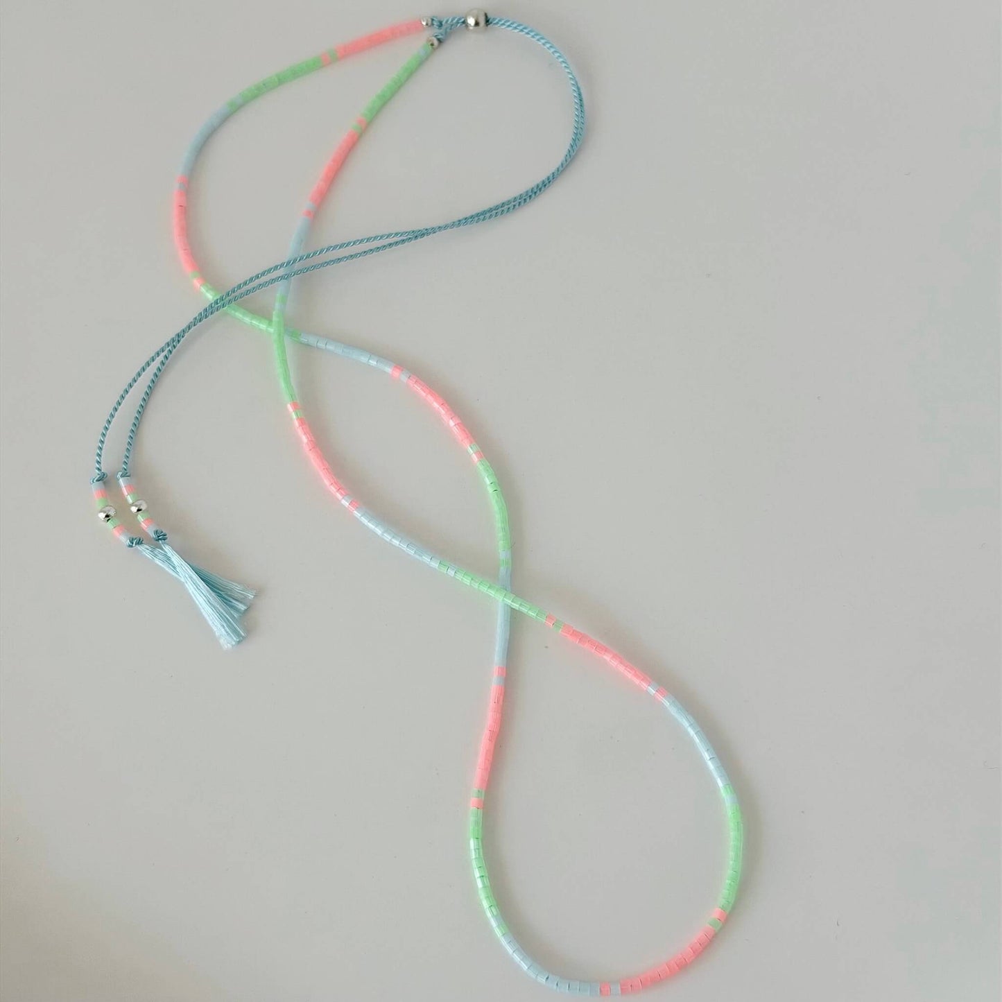 Dainty green, pink and pale blue glass bead necklace with sterling silver sliding clasp on a white flat lay surface