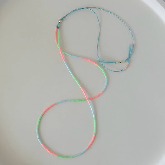 Dainty mint green, pink and pale blue glass bead necklace with sterling silver sliding clasp on a pale blue silk cord on a  white flat lay surface