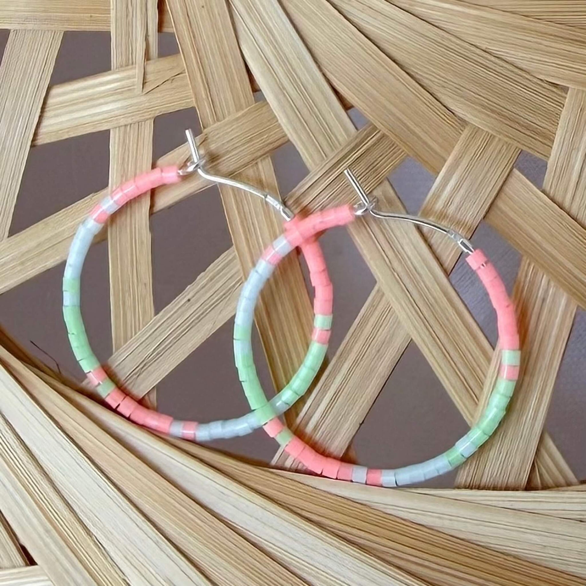 Beaded green, flamingo pink and pale blue glass sterling silver hoop earrings on a rattan background