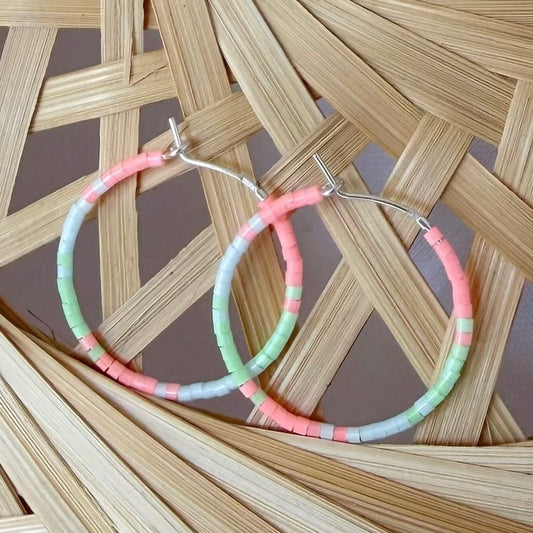 Beaded green, flamingo pink and pale blue glass sterling silver hoop earrings on a rattan background