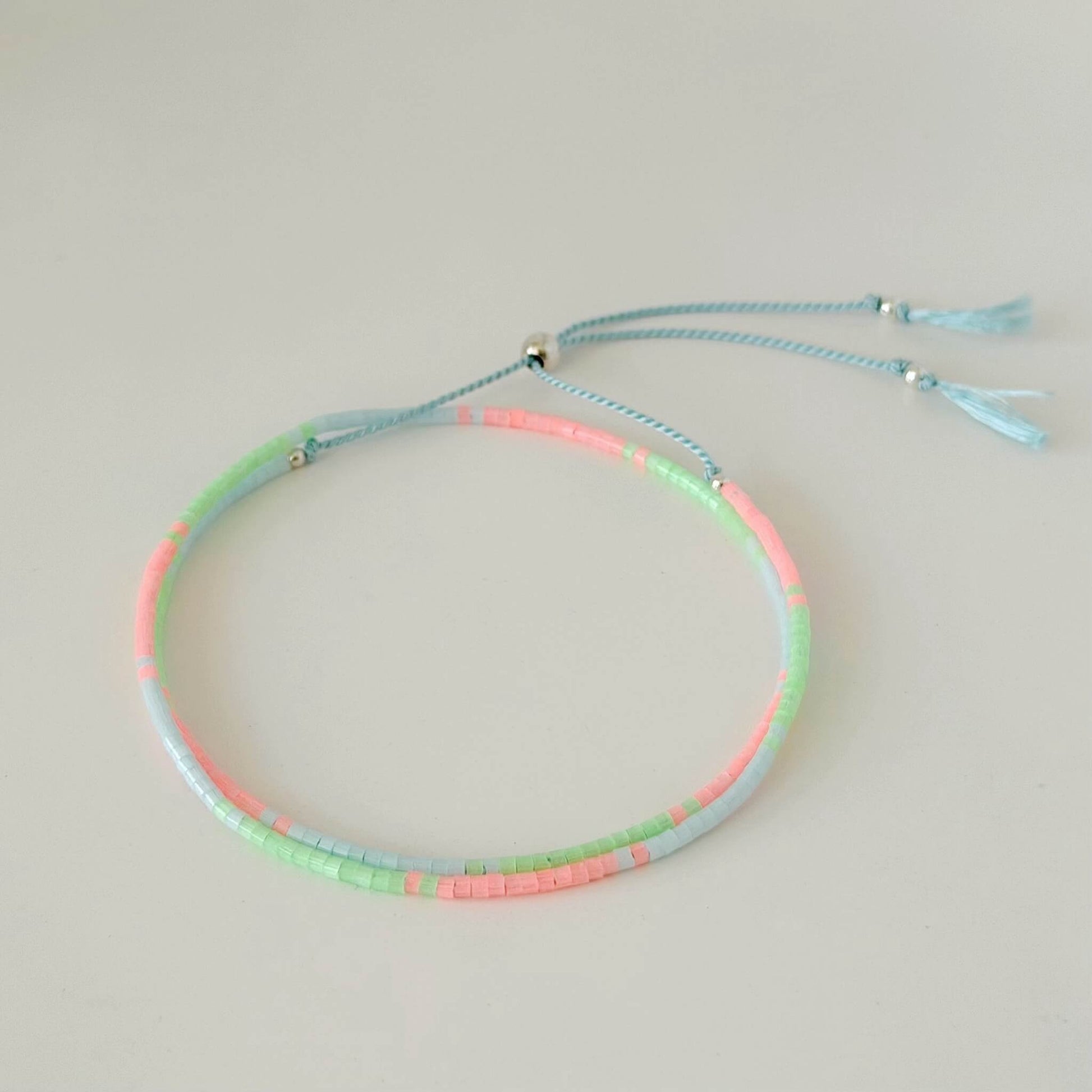 beaded double wrap green, pink and pale blue glass bead bracelet with sterling silver sliding clasp on a neutral surface
