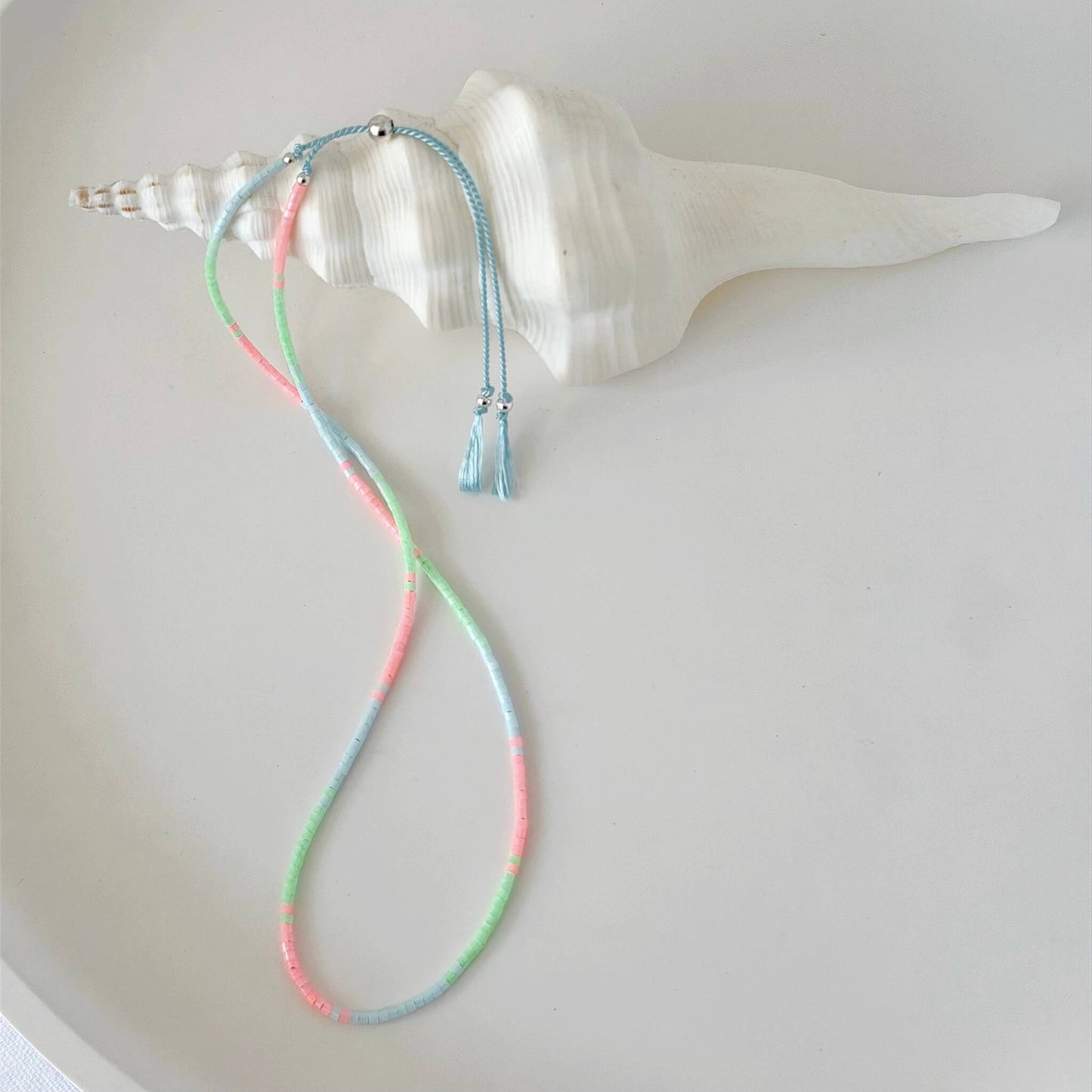 Dainty double wrap green, pink and pale blue glass bead bracelet with sterling silver sliding clasp on a neutral surface with white shell