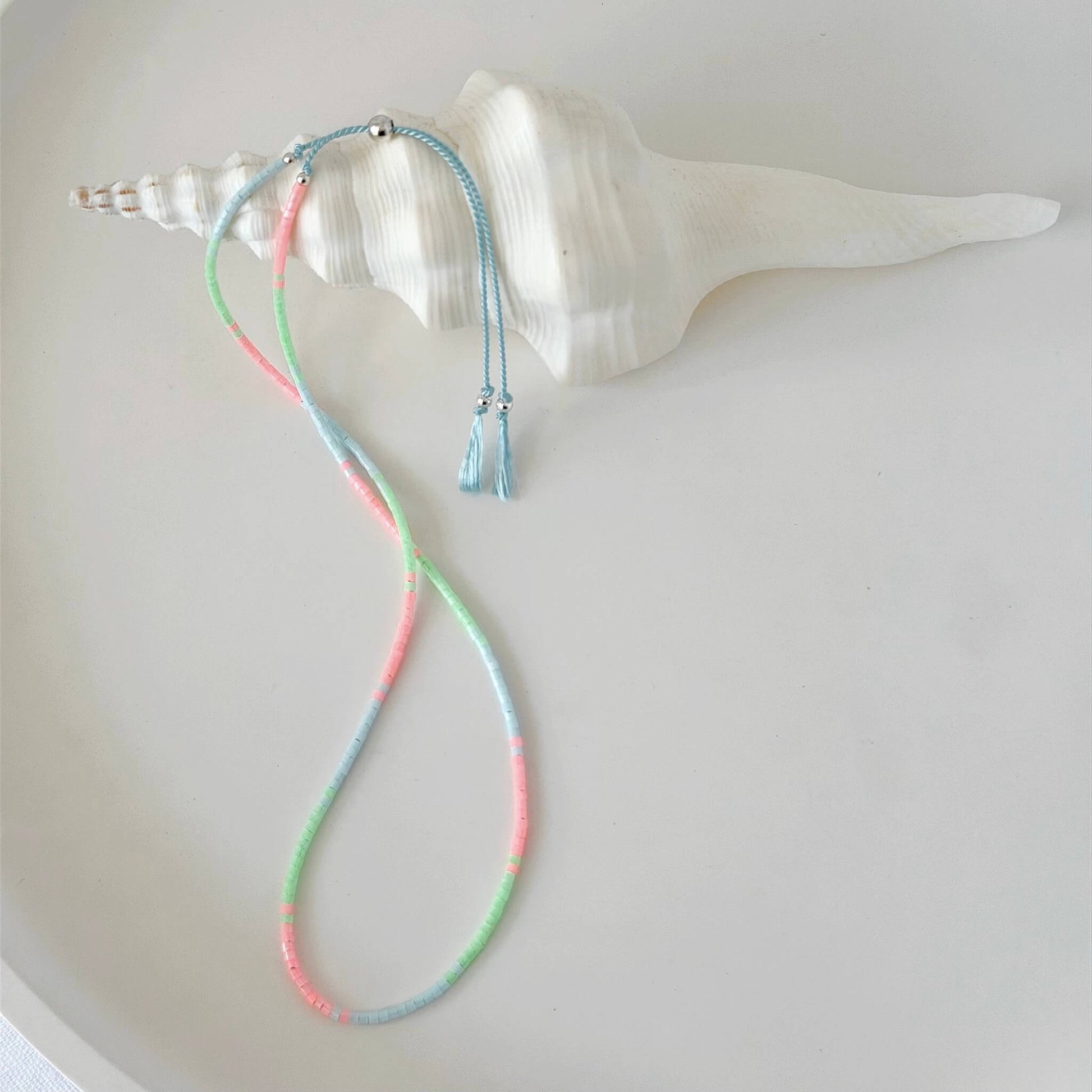 Dainty double wrap green, pink and pale blue glass bead bracelet with sterling silver sliding clasp on a neutral surface with white shell