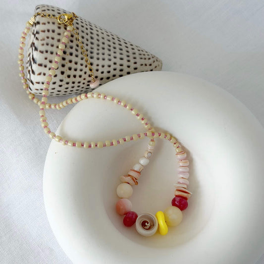 Yellow, pale gold, pink and red shell and glass bead necklace with gold fill clasp on a white bowl background